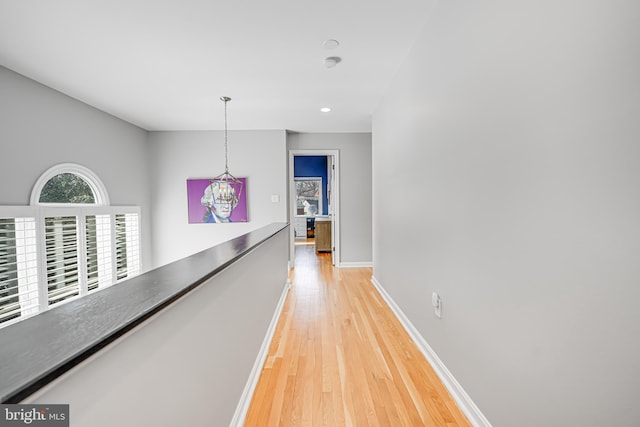 hallway with baseboards, an upstairs landing, and light wood finished floors