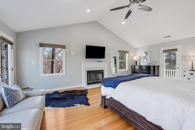 bedroom with access to exterior, visible vents, light wood finished floors, a fireplace with flush hearth, and lofted ceiling