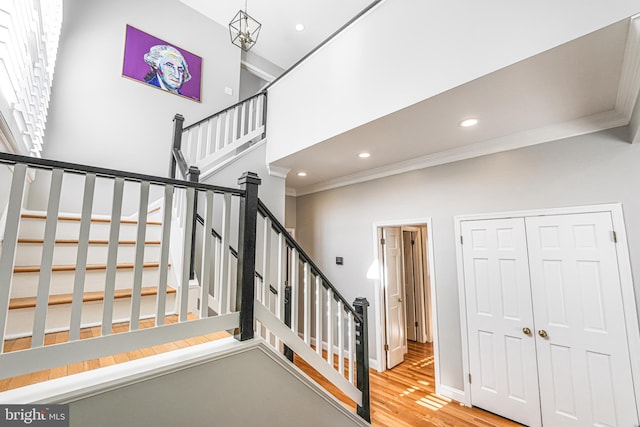 stairs with wood finished floors, baseboards, a high ceiling, recessed lighting, and crown molding