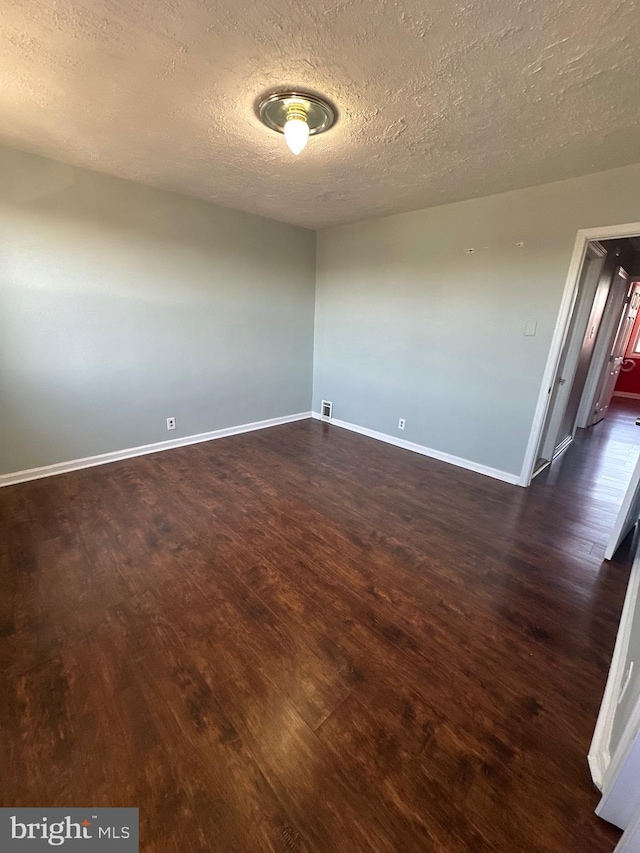 empty room featuring visible vents, baseboards, dark wood-type flooring, and a textured ceiling