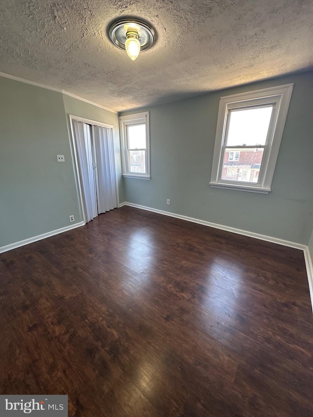 spare room featuring baseboards, a textured ceiling, wood finished floors, and crown molding