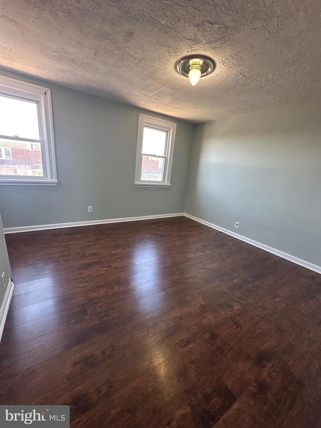 empty room featuring a textured ceiling, baseboards, and dark wood-style flooring