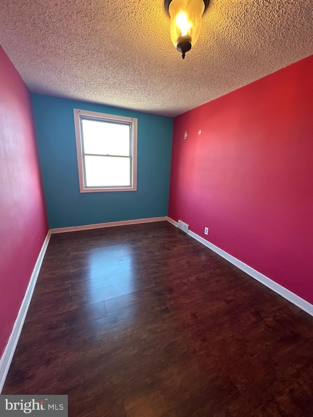 spare room featuring visible vents, baseboards, a textured ceiling, and wood finished floors