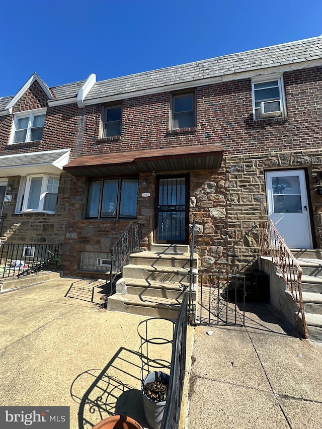 view of front of house featuring a high end roof, cooling unit, and brick siding