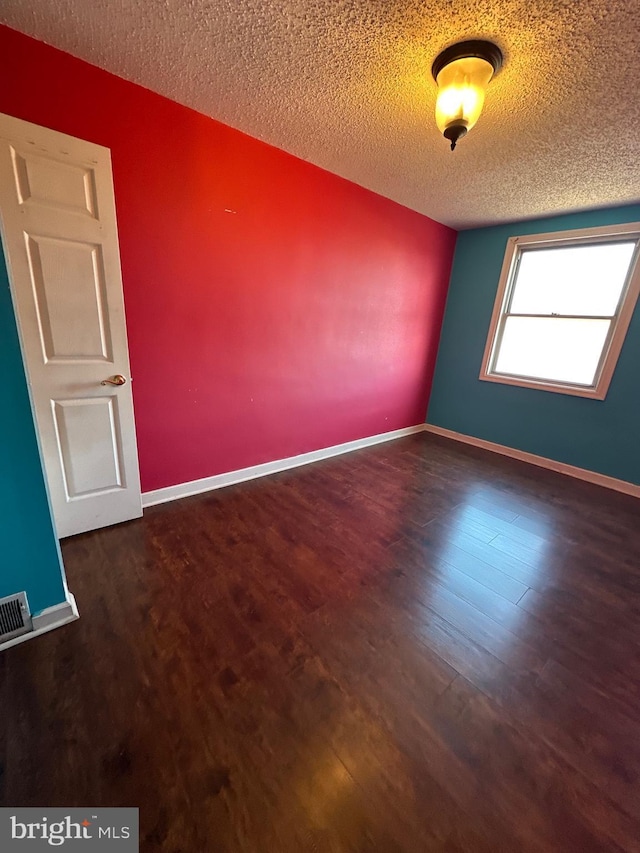 spare room with visible vents, a textured ceiling, baseboards, and wood finished floors