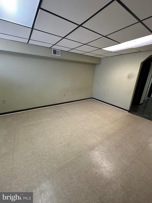 finished below grade area featuring tile patterned floors, a paneled ceiling, visible vents, and baseboards