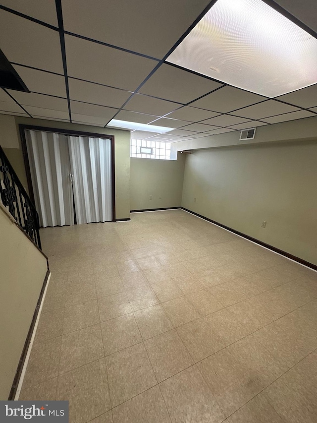 below grade area featuring tile patterned floors, a drop ceiling, baseboards, and visible vents