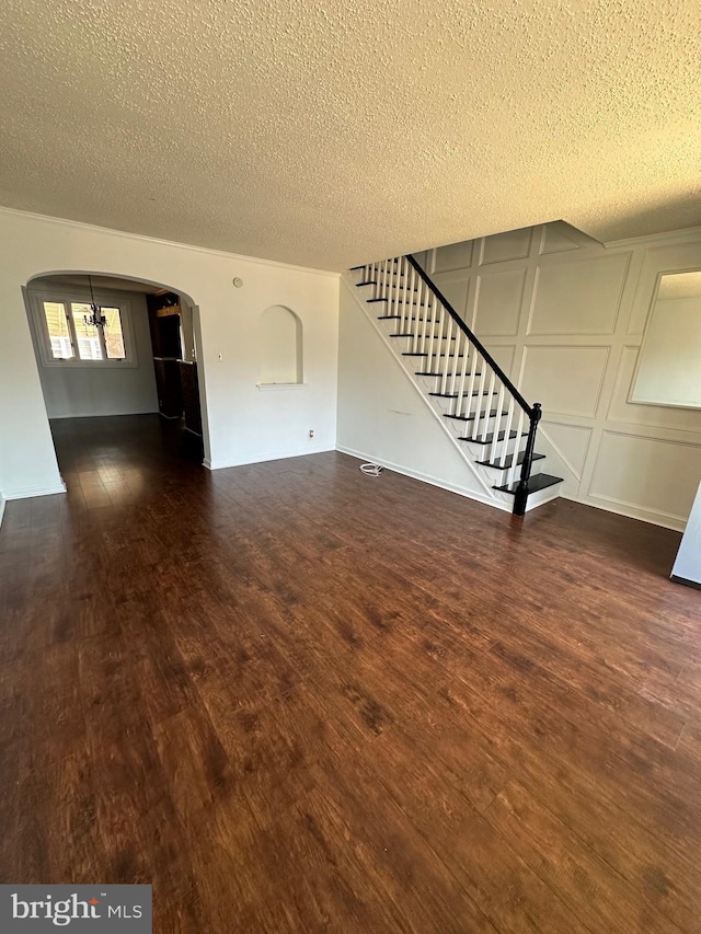 unfurnished living room featuring arched walkways, a decorative wall, stairs, and wood finished floors