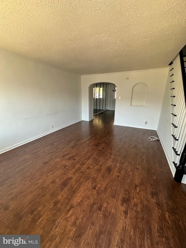 unfurnished living room with dark wood-style floors, baseboards, arched walkways, stairs, and a textured ceiling