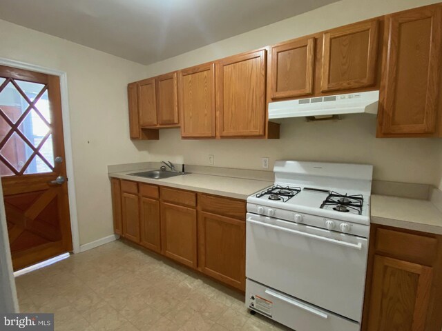 kitchen with under cabinet range hood, white gas stove, light floors, light countertops, and a sink