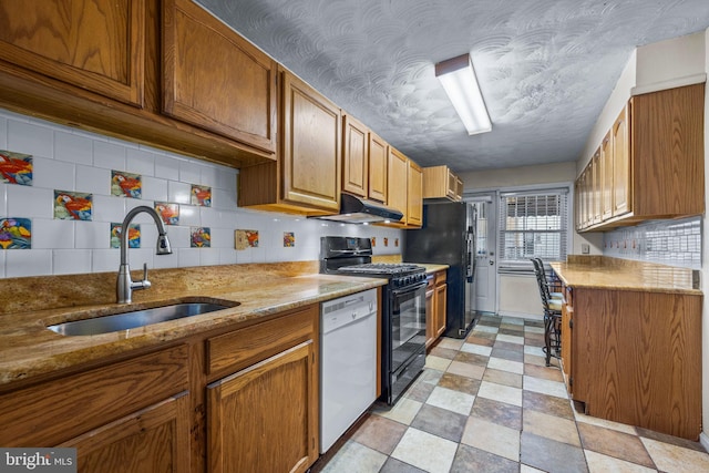 kitchen featuring black appliances, a sink, light stone counters, under cabinet range hood, and light floors