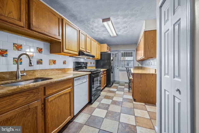 kitchen with light stone counters, a sink, black appliances, under cabinet range hood, and tasteful backsplash