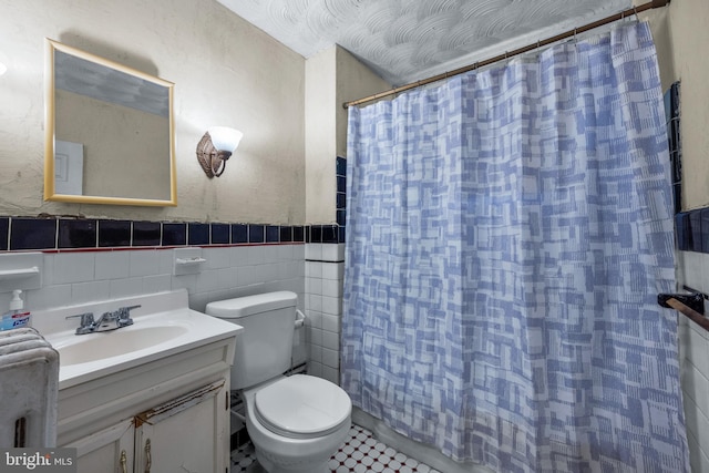 bathroom featuring vanity, a shower with shower curtain, a wainscoted wall, tile walls, and toilet