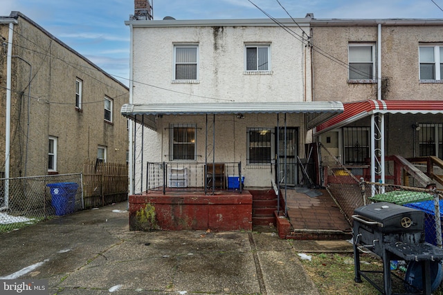 rear view of property featuring stucco siding, covered porch, and fence