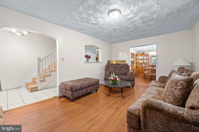 living area featuring stairway, arched walkways, a textured ceiling, and wood finished floors