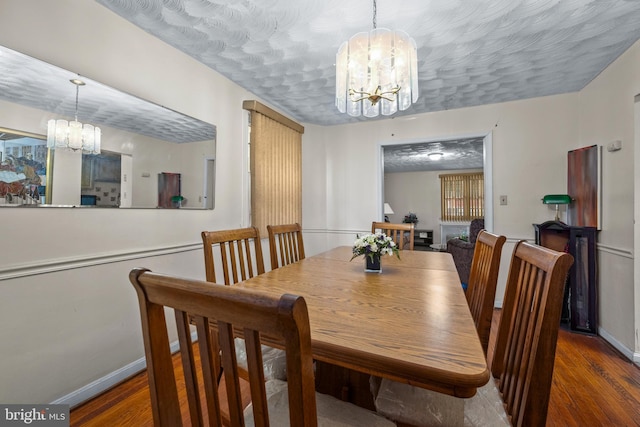 dining space featuring a textured ceiling, wood finished floors, baseboards, and a chandelier