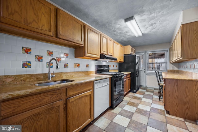 kitchen with black appliances, a sink, under cabinet range hood, backsplash, and light floors