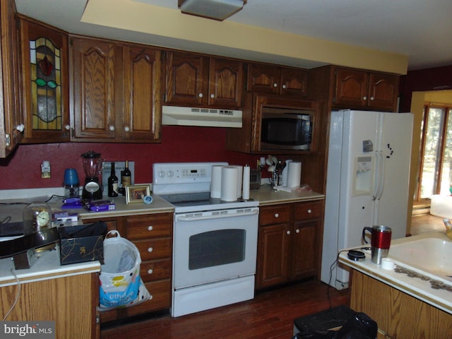 kitchen featuring under cabinet range hood, dark wood finished floors, white appliances, and light countertops