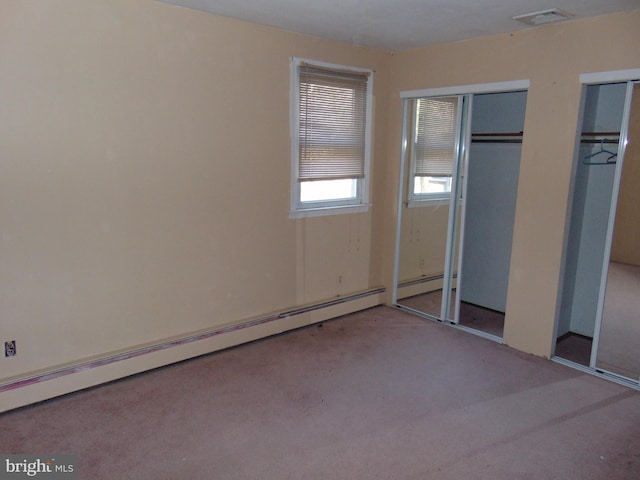 unfurnished bedroom featuring baseboard heating, carpet, visible vents, and multiple closets