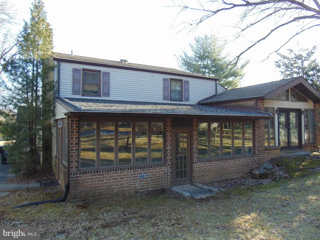 exterior space featuring brick siding, a sunroom, and a shingled roof