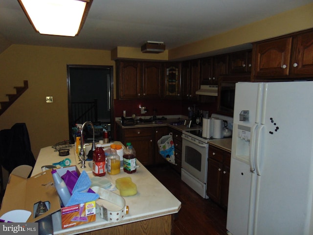 kitchen with under cabinet range hood, dark wood finished floors, white appliances, and light countertops