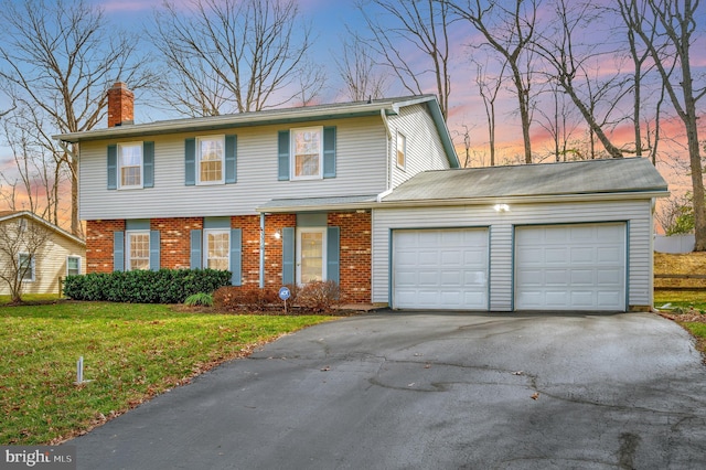 colonial-style house with a lawn, driveway, an attached garage, brick siding, and a chimney