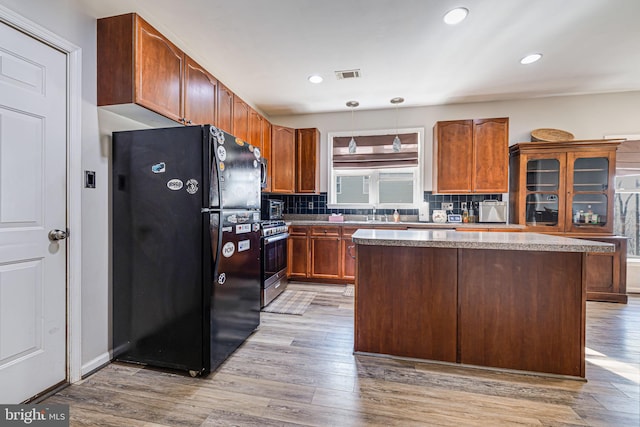 kitchen with stainless steel gas stove, visible vents, light wood-type flooring, and freestanding refrigerator