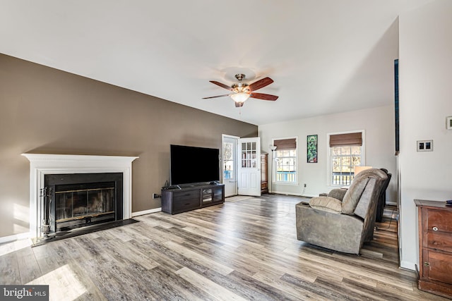 living area featuring a fireplace with flush hearth, baseboards, ceiling fan, and wood finished floors