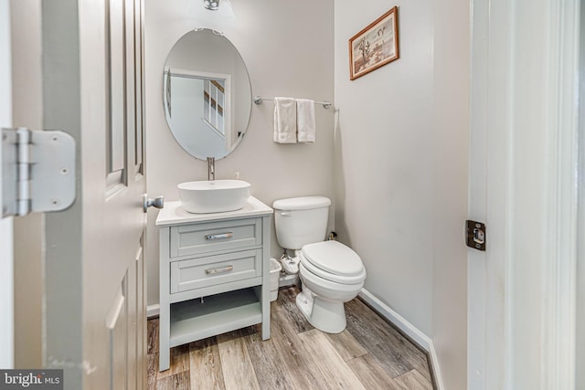 half bath with vanity, toilet, wood finished floors, and baseboards