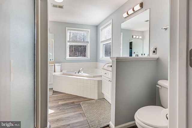 full bathroom with a garden tub, toilet, wood finished floors, and visible vents