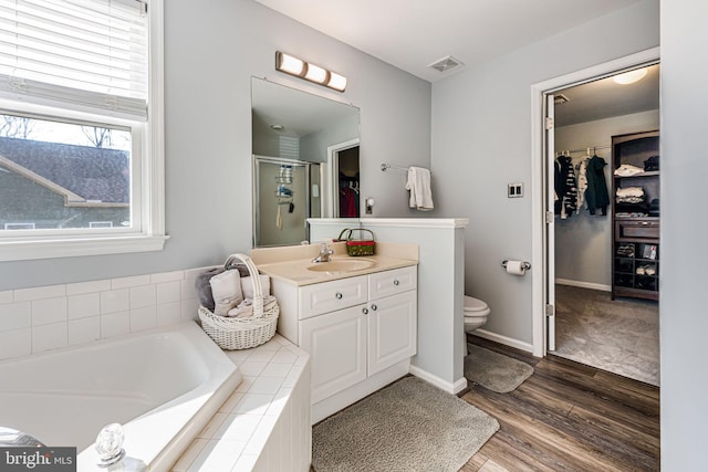 full bath with visible vents, vanity, a walk in closet, and wood finished floors