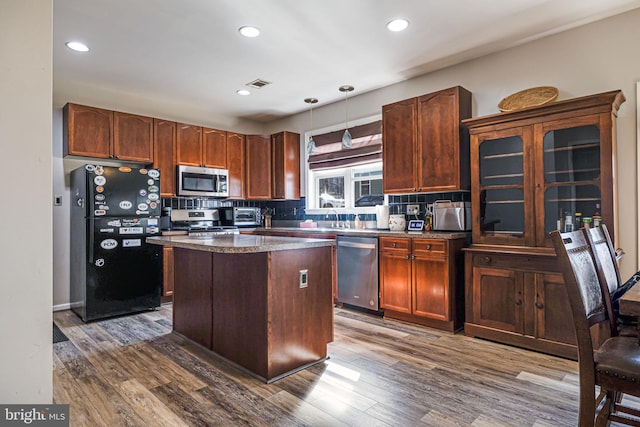 kitchen featuring visible vents, a kitchen island, dark wood finished floors, stainless steel appliances, and decorative backsplash