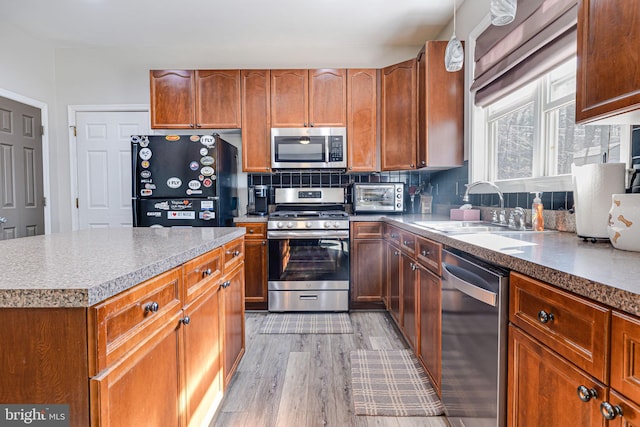 kitchen featuring light wood-style flooring, a sink, tasteful backsplash, stainless steel appliances, and a toaster