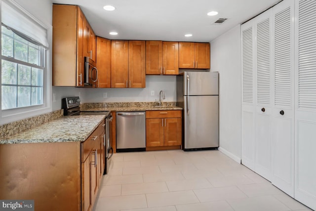 kitchen with brown cabinetry, visible vents, light stone counters, a sink, and stainless steel appliances