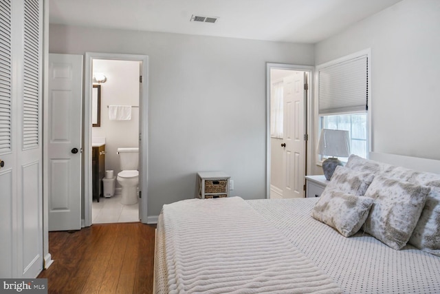 bedroom with a closet, ensuite bath, visible vents, wood-type flooring, and baseboards