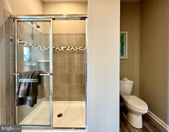 bathroom with baseboards, wood finished floors, toilet, and a stall shower