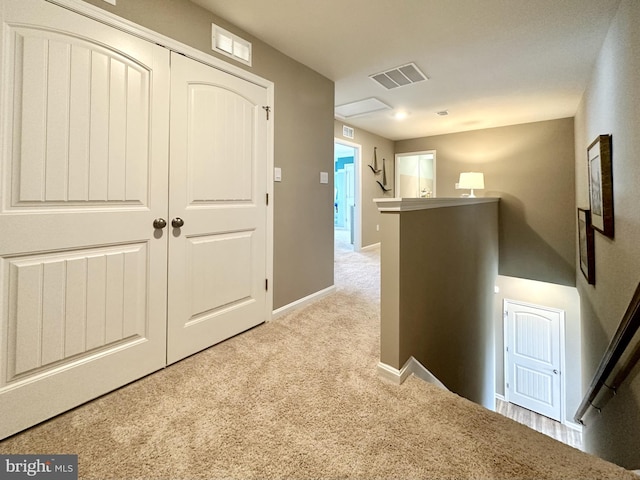 hall with an upstairs landing, visible vents, light colored carpet, and baseboards