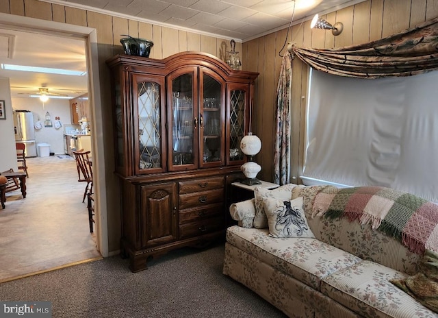 living area with wood walls, light colored carpet, a ceiling fan, and ornamental molding