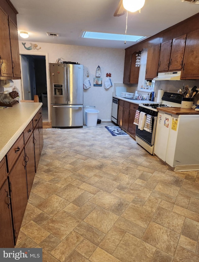 kitchen with stone finish floor, under cabinet range hood, range with gas cooktop, stainless steel fridge, and light countertops