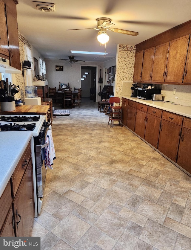 kitchen with visible vents, brown cabinets, range with gas stovetop, light countertops, and ceiling fan