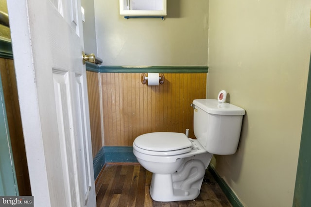 bathroom featuring wooden walls, toilet, baseboards, and wood-type flooring