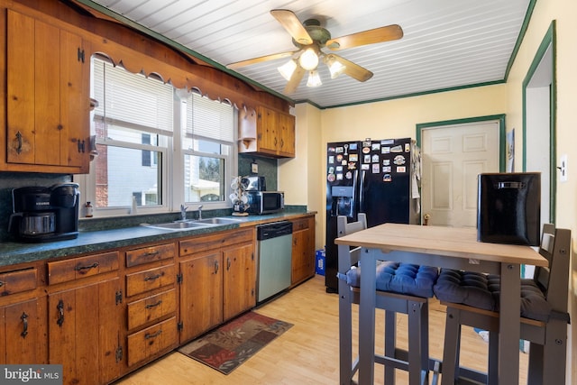 kitchen featuring light wood-type flooring, a sink, dark countertops, stainless steel appliances, and brown cabinetry