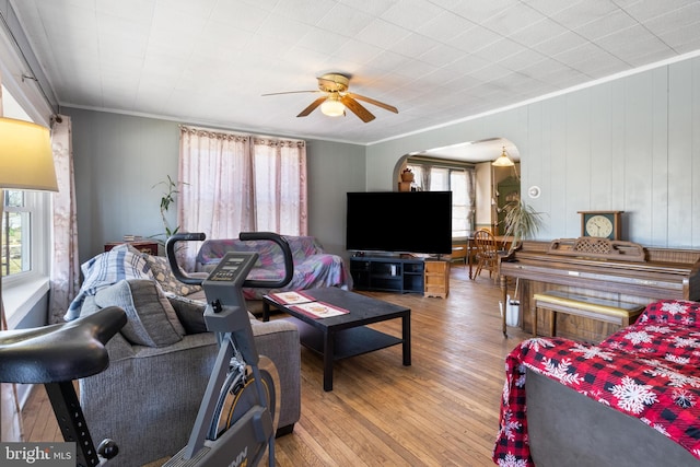 living area with arched walkways, wood finished floors, a ceiling fan, and ornamental molding