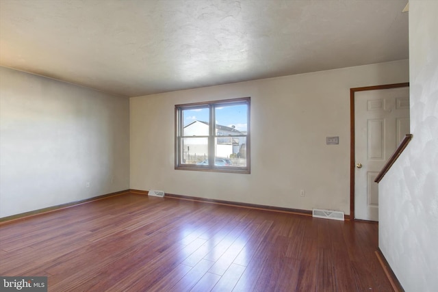 empty room featuring visible vents, baseboards, dark wood-style flooring, and stairway