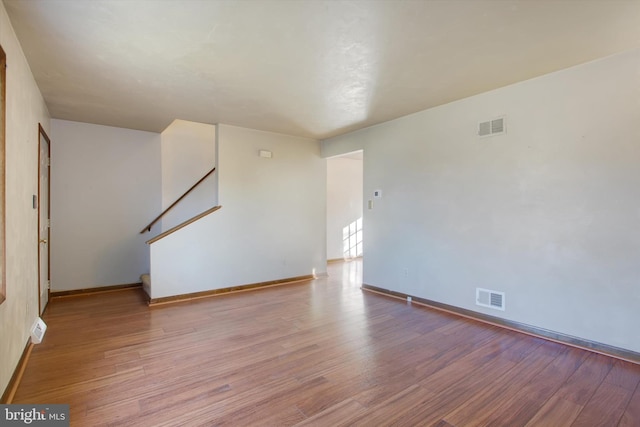 unfurnished living room with visible vents, stairway, and wood finished floors