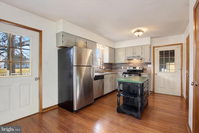 kitchen featuring decorative backsplash, under cabinet range hood, wood finished floors, and appliances with stainless steel finishes