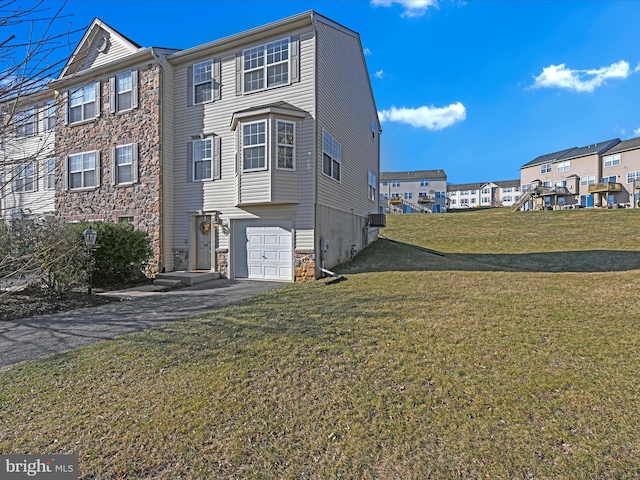 view of side of home with an attached garage, a lawn, stone siding, and driveway