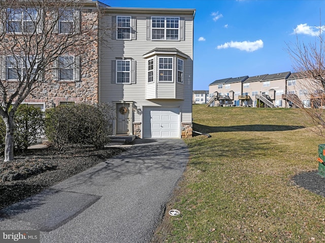 townhome / multi-family property with aphalt driveway, stone siding, a garage, and a front lawn