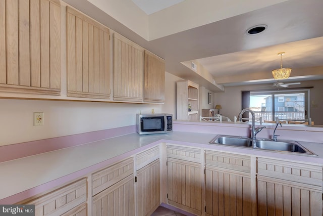 kitchen featuring light brown cabinets, a sink, light countertops, pendant lighting, and stainless steel microwave