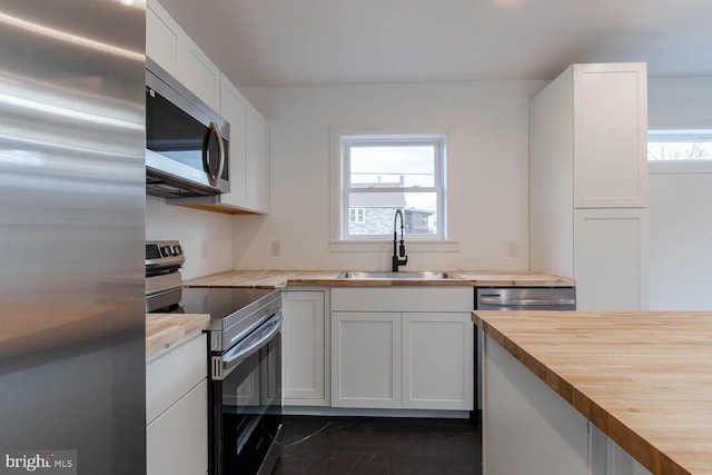 kitchen with white cabinets, appliances with stainless steel finishes, wood counters, and a sink